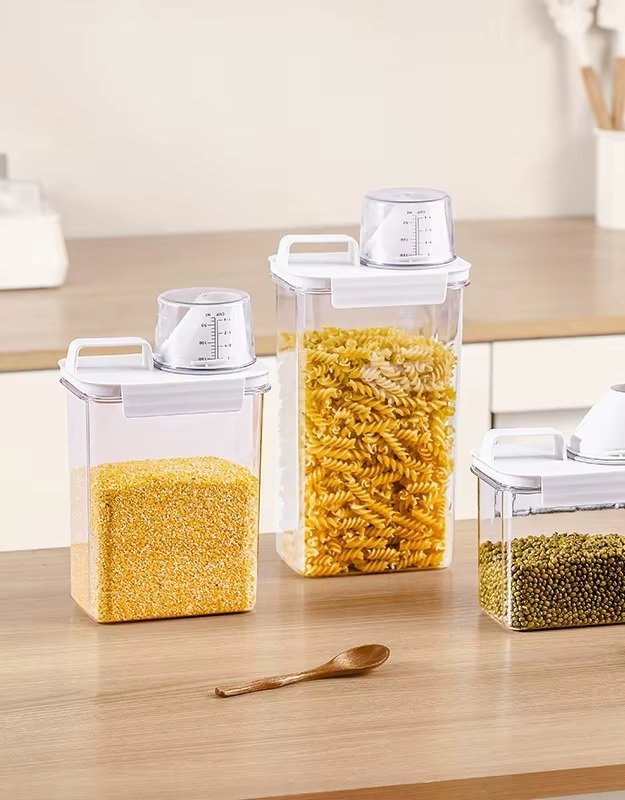 A set of transparent food storage containers with white lids, filled with various dry food items like pasta and grains, on a kitchen countertop.